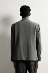 Blazer de corte relaxed fit color gris, confeccionado en tejido con lana. Cuenta con solapas de pico, manga larga con botones en los puños, bolsillos con solapa en la cadera y un bolsillo de vivo en el pecho. Presenta cierre frontal de botonadura cruzada con botones oscuros.