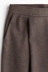 Pantalón de punto color marrón oscuro, de tiro alto, corte ancho y piernas amplias. Presenta pinzas frontales y bolsillos al bies.