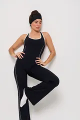 Mono deportivo de una pieza en color negro, con diseño de corte ajustado en el torso y piernas ligeramente acampanadas. Presenta detalles de líneas blancas contrastantes a lo largo de los laterales y en el escote, con espalda estilo nadadora.