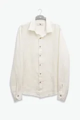 Camisa de manga larga color blanco hueso, confeccionada en lino, con cuello clásico y cierre frontal con botones de coco.