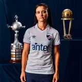 Camiseta de fútbol Umbro del Club Nacional de Football, modelo Home 2026, para mujer. Diseño en color blanco con sutil estampado jacquard, cuello tipo polo con detalles en azul y rojo, y logo de Umbro junto al escudo del club en el frente.
