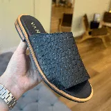 Sandalias chatas negras con diseño reptil, suela plana con borde color madera y plantilla con inscripción de la marca.