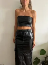 Falda midi de cuero sintético color negro, con corte recto, abertura frontal, bolsillos cargo laterales y cierre con botón y cremallera.