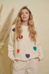 Buzo de punto color crema con diseño de corazones de colores aplicados en relieve, cuello redondo y mangas largas con puños acanalados.