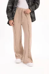 Pantalón de tejido de punto color beige, de corte recto y holgado, con cintura elástica con cordón ajustable y detalle de costuras desflecadas verticales en el frente.