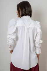 Camisa de algodón color marrón con mangas largas abullonadas, cuello clásico y cierre frontal oculto. Presenta botones decorativos con strass en los puños y en el cuello.