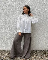 Camisa blanca de algodón con detalles de bordado inglés y calados en el canesú. Presenta cuello alto, cierre frontal de botones y mangas largas con puños terminados en volados bordados.