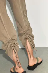 Pantalón de tiro medio confeccionado en tejido fluido color tostado. Presenta bolsillos de plastrón en el delantero y en la pierna, solapas en la espalda y detalle de frunces ajustables en el bajo. Cierre frontal con cremallera y botón.