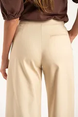 Pantalón de corte baggy y tiro medio, confeccionado en algodón peinado de color arena. Presenta diseño de pierna ancha, cierre frontal con botón y bolsillos laterales.