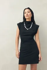 Vestido corto de punto color negro, sin mangas, con cuello cerrado y hombros levemente estructurados. Presenta frunce lateral que realza la figura.
