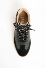 Zapatilla urbana de caña baja, con capellada combinada en tonos verde oscuro, marrón y negro. Presenta puntera y talón en gamuza negra, detalles en cuero marrón en el lateral y forro interior color beige. La suela es de goma color caramelo.