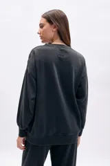 Buzo oversize negro con efecto desgastado, cuello redondo y estampado frontal de alas con la frase "Wild Hearts".