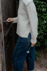 Buzo de punto color crema, con cuello polo y cierre frontal parcial con dos botones oscuros. Presenta mangas largas con puños acanalados y un diseño holgado.