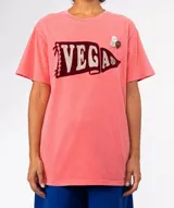 Remera de algodón color coral desgastado, con cuello redondo y manga corta. Presenta un estampado frontal de banderín con la palabra "VEGAS" en glitter. Tiene dos apliques decorativos (un pin redondo y dos púas de guitarra) prendidos en la zona superior derecha del pecho.