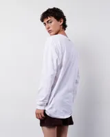 Remera blanca de manga larga, confeccionada en algodón. Presenta un estampado rectangular con una ilustración de un hombre con su caballo en un paisaje montañoso.