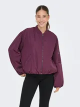 Campera bomber oversize color mauve wine, con cuello estilo baseball, cierre frontal con cremallera, bolsillo lateral y un bolsillo con cierre en la manga. Confeccionada en tejido plano con forro de poliéster.