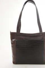 Cartera tipo tote de cuero vacuno negro con doble asa de hombro, panel superior liso y bolsillo exterior frontal con textura símil cocodrilo y costuras visibles en contraste.