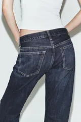 Pantalón de jean de tiro medio con corte recto y cinco bolsillos. Presenta un acabado con dobladillo ancho en el bajo y cierre frontal con botones metálicos.