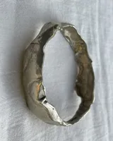 Brazalete rígido de diseño orgánico con textura irregular y acabado brillante, elaborado artesanalmente en metales nobles.