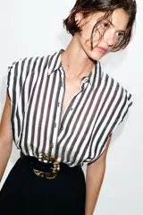 Vestido midi combinado con parte superior de camisa a rayas verticales blancas y negras, cuello solapa, manga sisa con frunces y botones dorados. La parte inferior es una falda midi negra de corte recto. Incluye un cinturón negro con textura de cocodrilo y hebilla dorada.