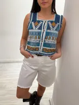 Chaleco corto en denim con bordado artesanal multicolor y escote cuadrado. Con cierre de botones y terminaciones desflecadas.