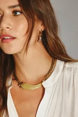 Collar dorado con cadena de eslabones gruesos y un dije central en forma de cuerno curvo de resina color verde claro.