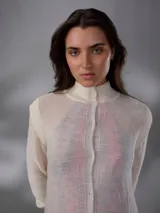 Saco largo de punto color blanco, confeccionado en 100% lana merino natural, con diseño jacquard de ramas, cuello alto, cierre frontal con pequeños botones y aberturas laterales.