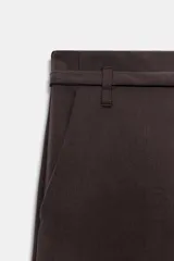 Pantalón de tiro bajo y corte recto, color marrón oscuro. Presenta bolsillos laterales, cierre frontal con cremallera y gancho metálico, y un cinturón integrado del mismo tejido con hebilla metálica.