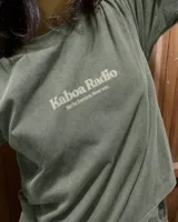 Remera oversize negra con diseño gráfico en la espalda que incluye la inscripción "Kaboa Radio" y un personaje ilustrado, de corte amplio y mangas cortas.