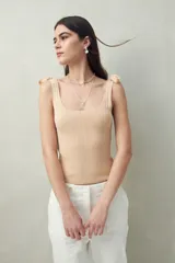Top tejido color beige claro, ajustado al cuerpo, con escote cuadrado y tiras para anudar en los hombros. Presenta textura acanalada vertical.