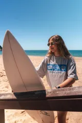 Remerón cropped color hueso con estampado frontal de tres cuadrados azules que contienen un hibisco, una ola y una concha marina, y la frase "Glassy Waves".