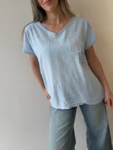 Remera de lino y algodón color beige con escote en V, mangas cortas y calce relajado. Presenta un bolsillo frontal decorado con apliques de strass, encaje y tachas, además de sutiles estampas con escritura manuscrita y detalles desflecados.