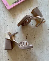 Sandalia de cuero vacuno color beige, con plataforma y taco cuadrado alto. Presenta un diseño de tiras cruzadas en el empeine y cierre con pulsera ajustable al tobillo.