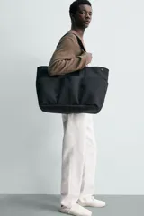 Bolso shopper negro fabricado en tejido técnico, con compartimento principal con cierre de botón a presión, múltiples bolsillos exteriores frontales, doble asa de mano y asas largas de hombro.