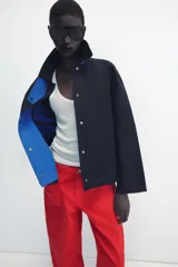 Chaqueta de Zara Woman Collection color negro, de cuello con solapa y manga larga. Cuenta con bolsillos delanteros ocultos en las costuras, cierre frontal con botones metálicos a presión y detalle de diseño asimétrico en azul en el cuello.