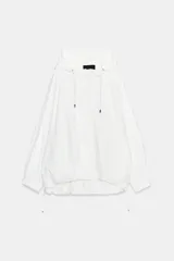 Chaqueta técnica de corte oversize en color blanco, con capucha ajustable mediante cordones, cierre frontal con cremallera y botones ocultos, mangas largas con puños elásticos y bajo asimétrico con cordón ajustable.