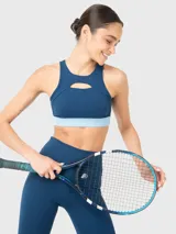 Top deportivo de entrenamiento con diseño de cuello alto y detalle de apertura frontal sobre el busto. Presenta una banda elástica inferior en tono celeste contrastante y almohadillas removibles.