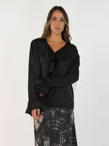Blusa de satén color negro con cuello en V, detalle de volados en el escote y mangas largas con puños acampanados también con volados.