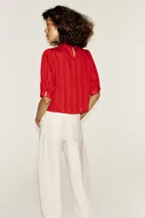 Blusa blanca de cuello alto con detalles de puntilla, manga corta abullonada y cierre posterior con botón.