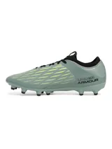 Championes de fútbol Under Armour Magnetico Select 4 FG, color verde grisáceo con detalles en amarillo neón y negro. Presentan una parte superior de piel sintética con estampado 3D para mayor control, cuello textil tipo calcetín y suela de TPU con tacos cónicos para tracción en césped natural.