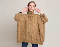 Tapado tipo poncho de tejido de punto grueso color beige, con cuello alto, cierre frontal con cremallera y bolsillos laterales.