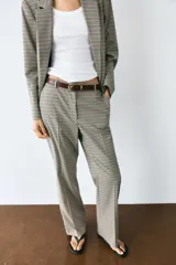 Pantalón de tiro alto color negro, de corte recto y pinzas frontales. Incluye un cinturón delgado de cuero marrón con hebilla metálica dorada.