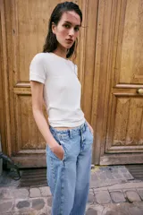 Jeans de tiro alto con corte barrel, pernera holgada que se estrecha hacia el tobillo y bajo deshilachado. Presenta costuras verticales decorativas en el frente y cierre frontal con cremallera y botón.