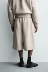 Bermuda de corte oversized confeccionada en tejido técnico compacto con elasticidad. Presenta cintura elástica ajustable con cordón, pinzas en el delantero y la espalda, y bolsillos laterales.