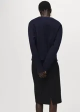 Cardigan de punto azul marino, con diseño cruzado, escote en V y cierre de un botón dorado en el lateral. Mangas largas abullonadas en los hombros.