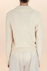 Sueter de punto color beige, con cuello polo, cierre frontal con botones y mangas largas con puños acanalados.