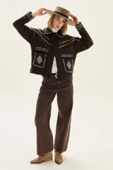 Campera de lana merino hervida en color crudo, con diseño de cuello camisero, cierre frontal de botones y bolsillos frontales. Presenta bordados artesanales con motivos geométricos en tonos marrón y azul en el frente, espalda y mangas.