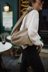 Bolso tipo hobo de cuero color beige, con asa anudada al hombro.