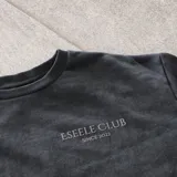 Buzo de cuello redondo Eseele Club Stone con acabado stonewash en color negro lavado, corte oversize y diseño relajado. Presenta logo ovalado retro en la espalda y terminaciones acanaladas.
