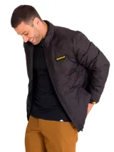 Chaqueta acolchada negra con cierre frontal, cuello alto y parche de silicona con logo Caterpillar en el pecho. Cuenta con aislamiento térmico, es resistente al agua y al viento, con ribetes elásticos en puños y dobladillo.